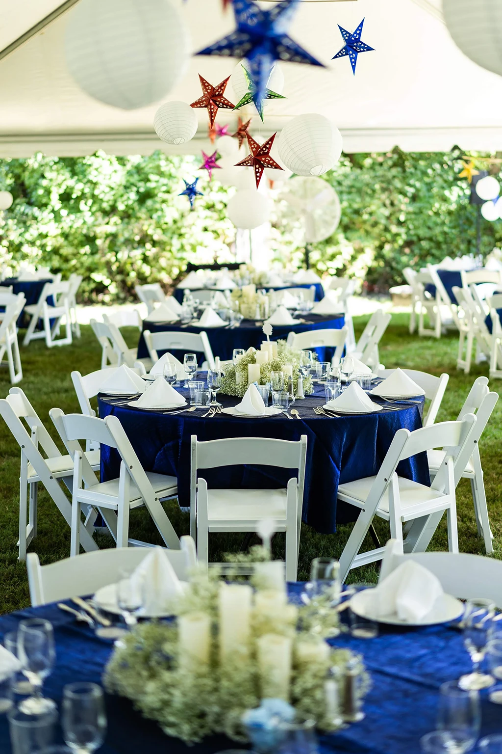 Tent reception with blue linens, white chairs, and hanging star lanterns