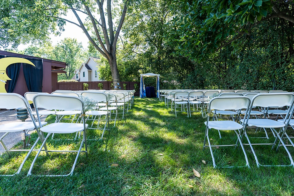 Outdoor wedding ceremony setup with white chairs and a small arbor